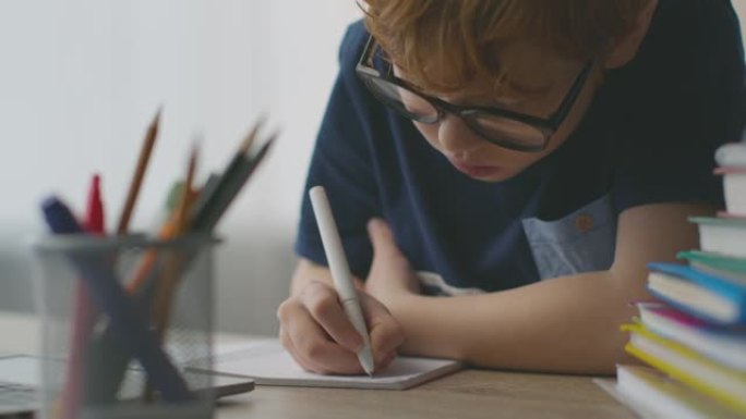 专心的小男孩学习写作，在家工作场所用笔记本写信，特写肖像，慢动作