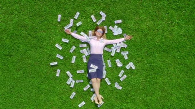戴着太阳镜的年轻美丽而成功的女商人躺在绿草如茵的草坪上，上面布满了钱。