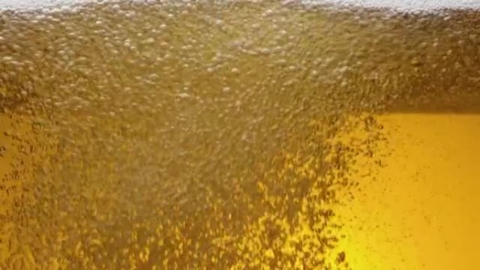 一杯啤酒内容物的特写。啤酒在玻璃，波浪，气泡和泡沫中缓慢地震动。