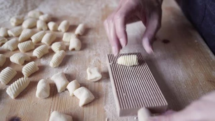 传统意大利面食自制素食汤团土豆制作过程的特写镜头。女人在木制规则板工具上煮面团。在家里玩得开心，用你
