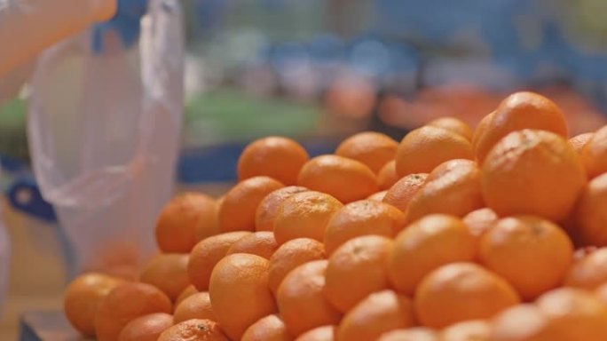 特写镜头，一只手戴着防护手套，拿起橘子，把它们放在袋子里。在超市买柑橘类水果。超市货架上有很多橘子。