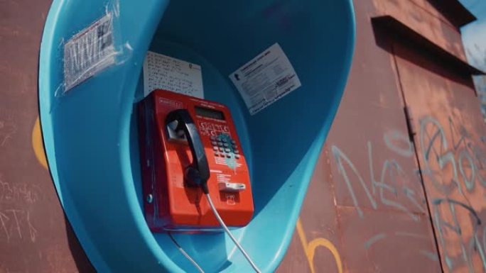一个蓝色的电话亭，里面有一个红色的电话亭，贴在生锈的金属墙上。