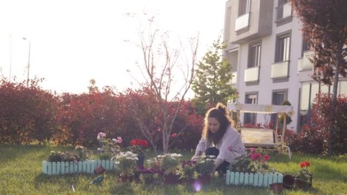 年轻女子园艺在一个阳光明媚的日子里，年轻女子正在房子的后院种花，双手种植绿色幼苗，社区园艺，都市农业