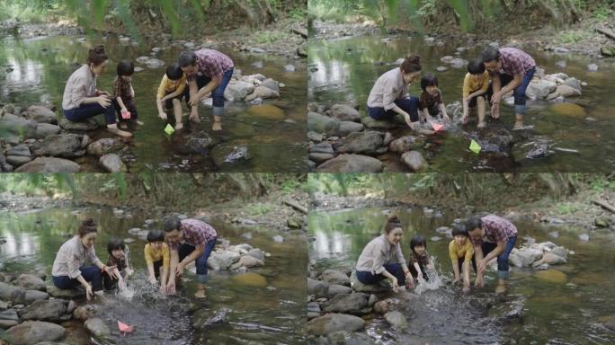慢动作，一个亚洲家庭，一个父亲和一个母亲教他们的两个儿子的孩子如何制作纸船。漂浮在天然森林溪流中。度
