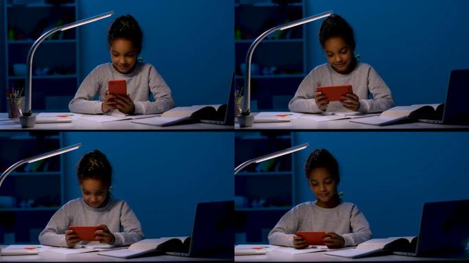 一个女孩把笔扔在桌子上，双臂交叉在胸前，然后拿起手机，玩游戏。孩子在夜灯的灯光下坐在桌子旁。特写。慢