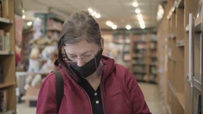 戴着眼镜和面具对抗病毒的女人从书店的书架上拿书