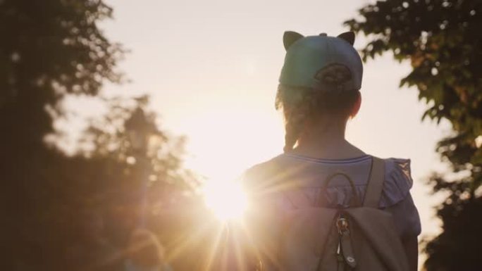 一个背着背包的孩子站在公园里，夕阳照在他身上