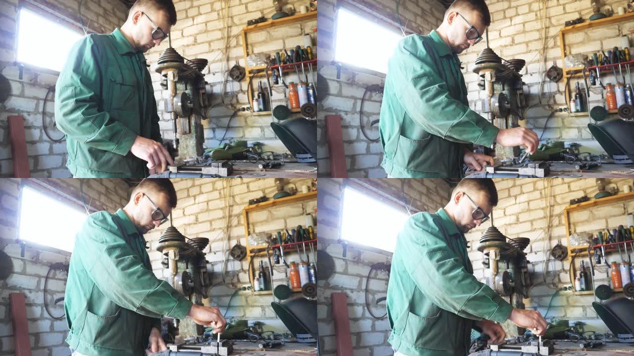 防护眼镜的男机械师在车间的桌子上固定金属细节。穿着制服的年轻修理工在车库工作。维护服务的概念。关闭慢