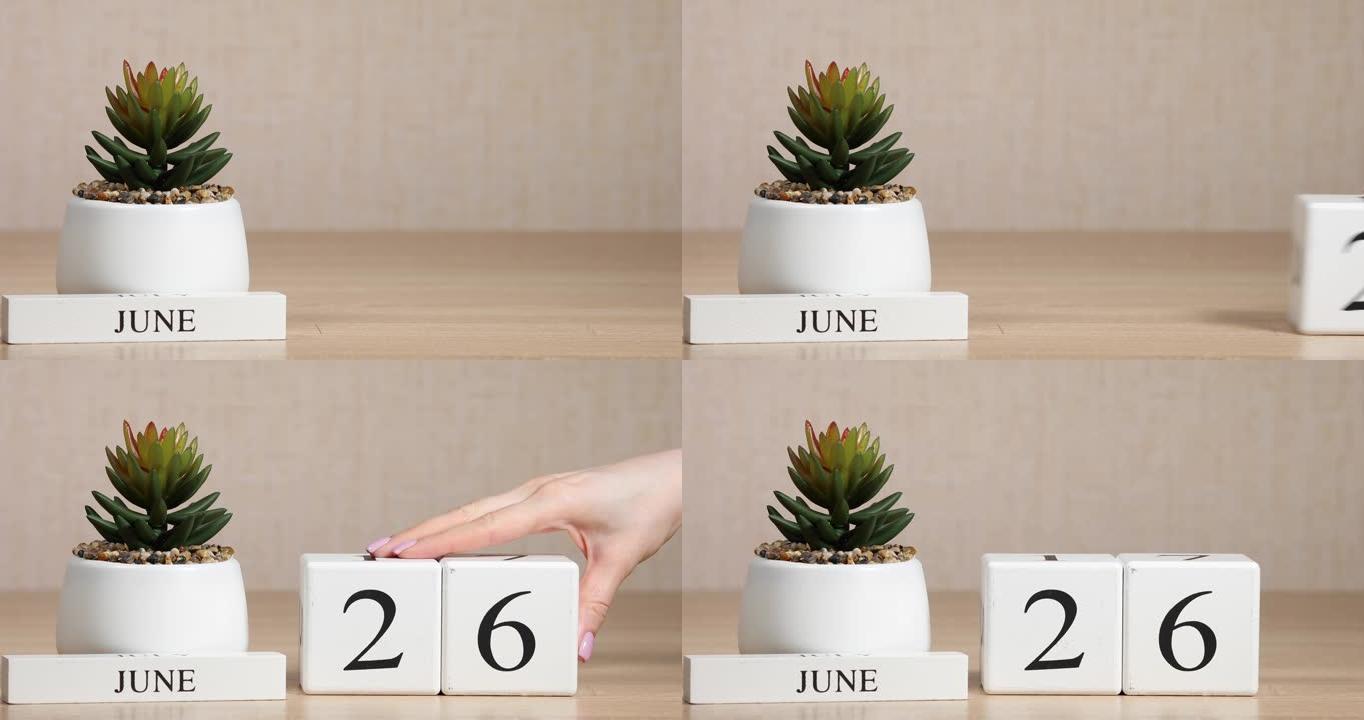 木制日历对6月26日来说是一个重要的事件，女人的手在日历上设置日期。夏季。