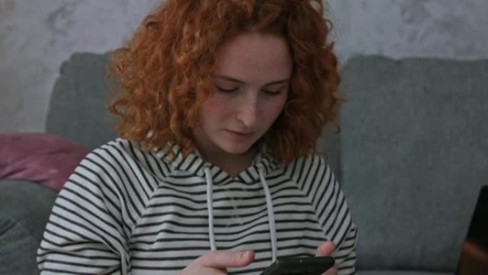 年轻的红发女郎写作业，被智能手机上的短信分散注意力