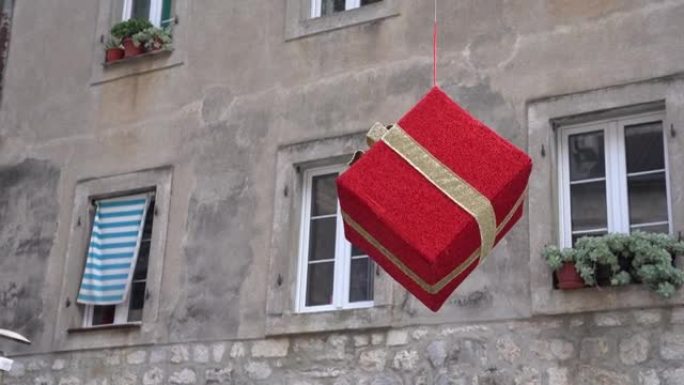 带有金色丝带的大型红色礼品盒挂在老式建筑的立面上，窗台上有窗户和植物。