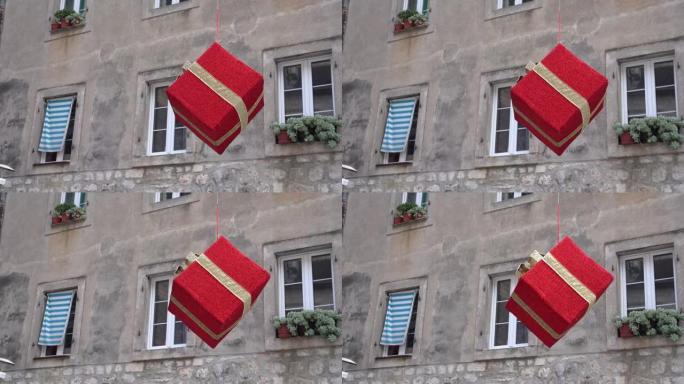 带有金色丝带的大型红色礼品盒挂在老式建筑的立面上，窗台上有窗户和植物。