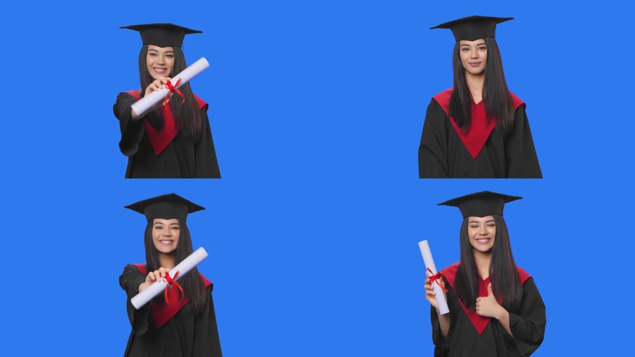 穿着帽裙毕业服装的女学生肖像，拿着文凭，竖起大拇指。年轻女子在工作室摆姿势，蓝屏背景。特写。慢动作准