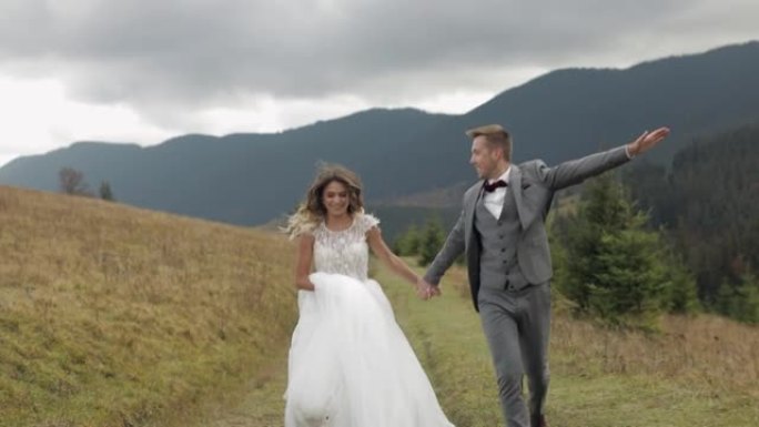 可爱的年轻新婚新娘新郎在山坡上奔跑，牵手，结婚夫妇家庭