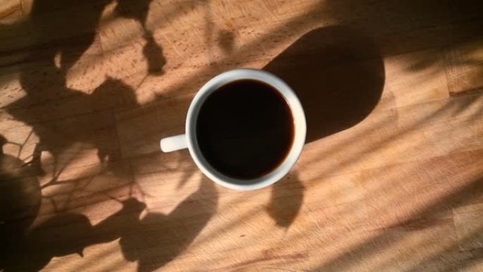 多莉拍摄了一个黑色咖啡杯，上面有天然蒸汽和气泡，在阳光明媚的早晨场景中从正上方拍摄