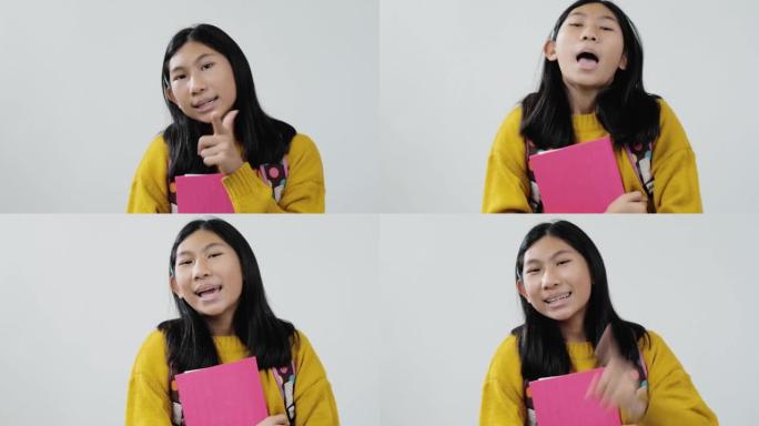 快乐的亚洲女学生穿着黄色毛衣，拿着粉色的书，在灰色背景上跳舞，生活方式理念。