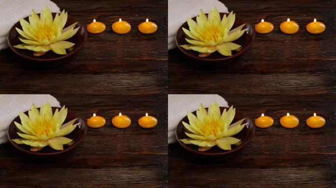 木桌上的黄莲睡莲花、毛巾和燃烧的蜡烛