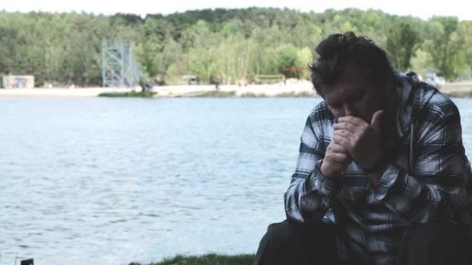 成熟的男人独自坐在湖岸上抽烟