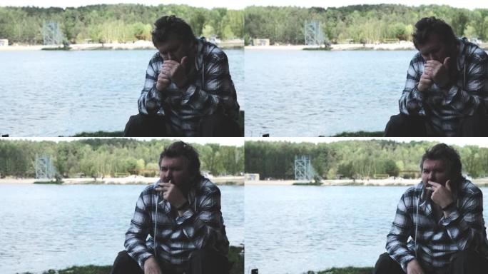 成熟的男人独自坐在湖岸上抽烟