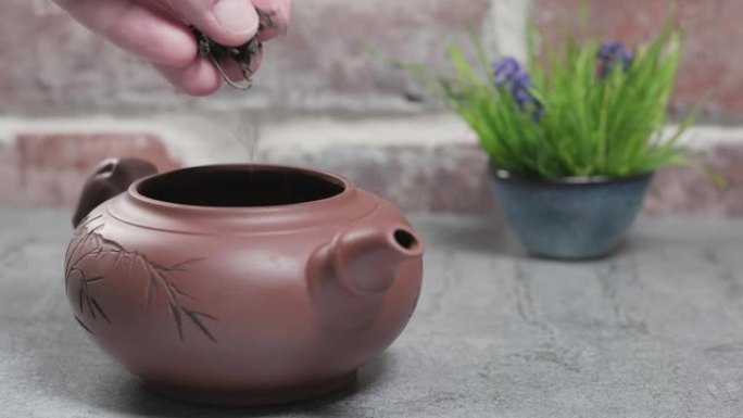 泡茶。将茶倒入位于灰色石桌上的粘土茶壶中。砖复古背景。特写，茶道，极简主义