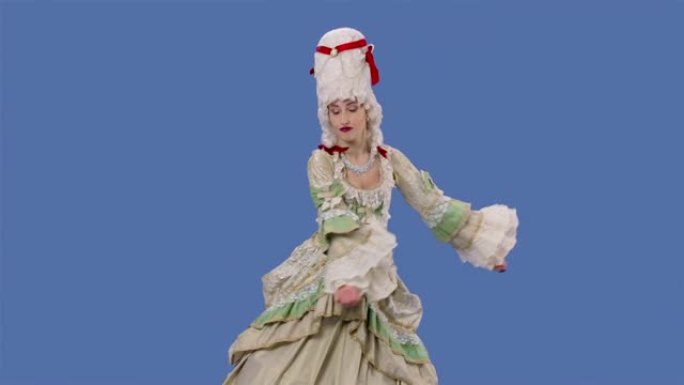 穿着白色复古蕾丝连衣裙和假发的朝臣女士的肖像正在欢快地跳舞。年轻女子在工作室摆姿势，蓝屏背景。慢动作