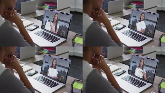 非裔美国女商人坐在办公桌前，用笔记本电脑与女同事进行视频通话