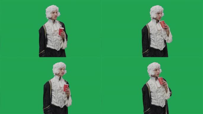 穿着复古西装和假发的朝臣绅士肖像，用塑料玻璃通过吸管喝饮料。年轻人在工作室摆姿势，绿屏背景。特写。慢