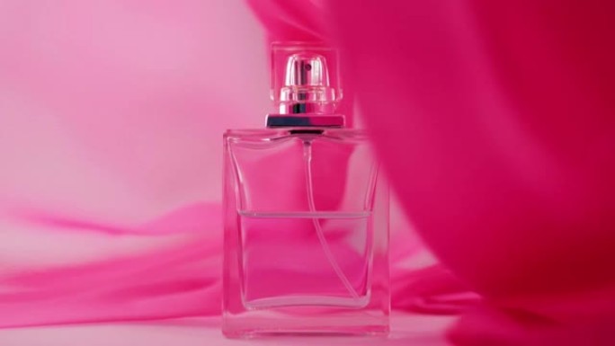 白色桌子上放着带有青色香水或精油的扁平瓶子。粉红色的织物四处飘动，瓶子周围的空气中飘扬。香气和气味的
