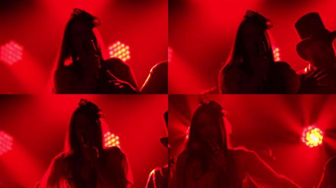 摇滚乐队女歌手的情感现场表演。一群音乐家在黑暗的工作室里，在红灯的背景下演奏乐器并向麦克风唱歌。剪影