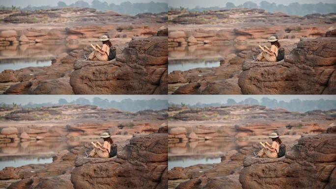 年轻的亚洲女探险家坐在大峡谷的岩石悬崖上看着纸质地图