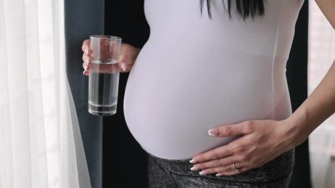 孕妇在家拿着一杯水站在窗边