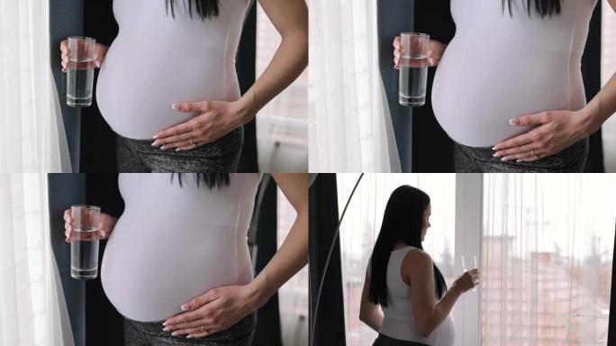 孕妇在家拿着一杯水站在窗边
