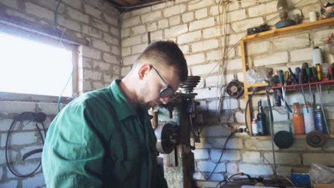 工作服的年轻修理工在车库检查车辆细节。疲惫的工人机械师脱下防护眼镜，擦去额头上的汗水。在车间工作的男