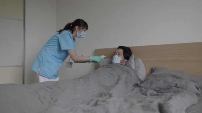 亚洲医务人员为病人量体温，而病人躺在家里的床上