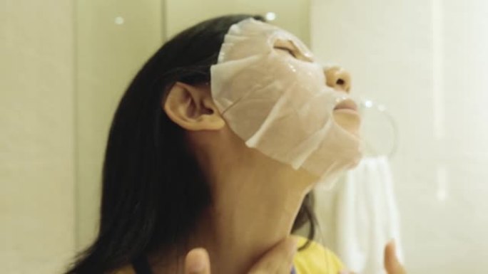 快乐的亚洲女孩在酒店度假期间睡觉前在浴室用面膜遮住脸，生活方式理念。