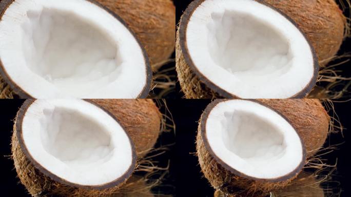 黑色背景上椰子分成两半的4k多莉视频。有机食品和健康营养的完美抽象镜头。热带水果特写