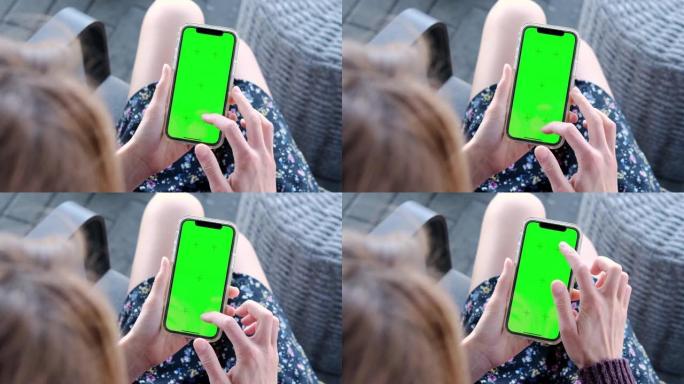 空白数字智能手机在女性手中。女孩坐在椅子上，用绿屏模拟颜色键在手机上聊天，上网观看视频。