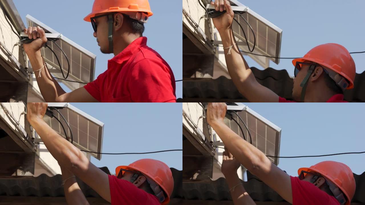亚洲人用钻头将太阳能电池板安装到金属基础上。他在阳光明媚的日子在房子的屋顶上工作。