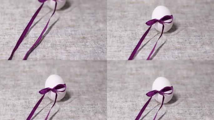 灰色背景上的紫色丝带蝴蝶结绑着鸡白蛋。春天和复活节