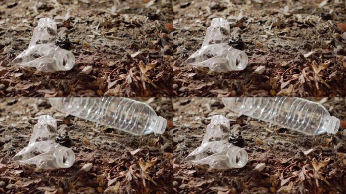 特写-塑料瓶扔在另一个留在土壤上的瓶子旁边。环境问题、土壤污染和垃圾填埋概念。
