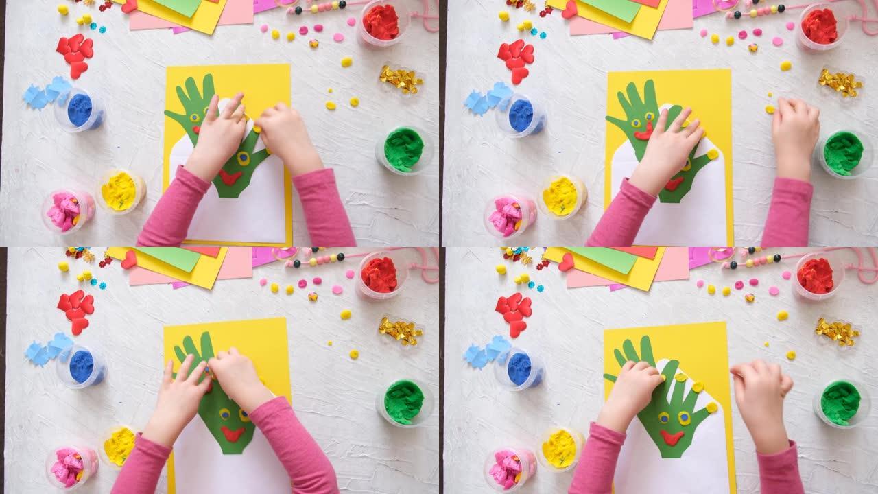 小女孩用信封、纸自己的手掌和装饰粘土、橡皮泥制作自制贺卡，作为母亲节、生日或情人节的礼物。工艺概念。