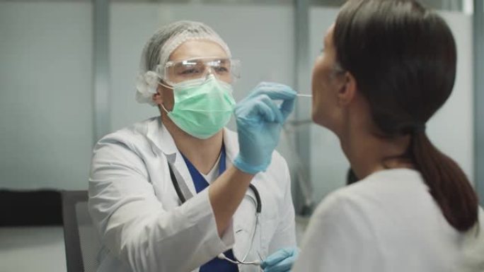 一名医生穿着医用长袍和手套对一名年轻患者进行PCR分析。检测冠状病毒的测试。大众人口调查