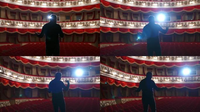 剧院舞台上的播音员。一个人身上明亮的圆形光线。穿着黑色西装的男子在礼堂表演。从后面看。