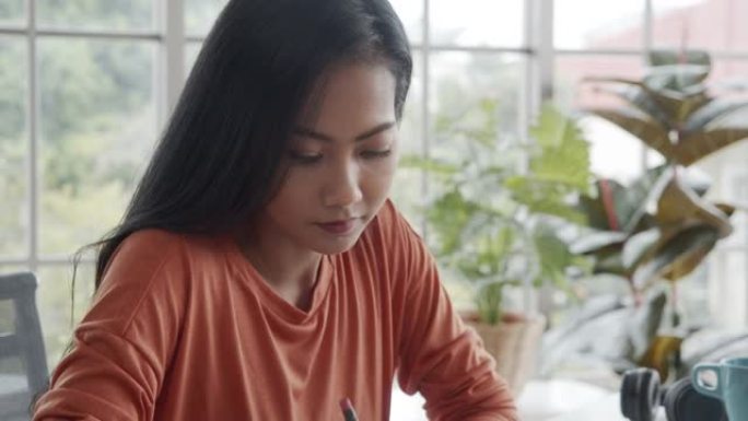 亚洲创意女性在家工作时在笔记本上写下规划大项目的想法。