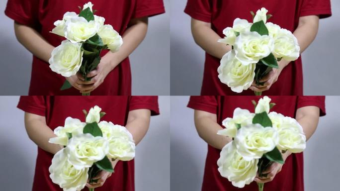 闭合女性双手，手持五颜六色的玫瑰花束。女人手触摸玫瑰花蕾叶，白色针织毛衣背景。