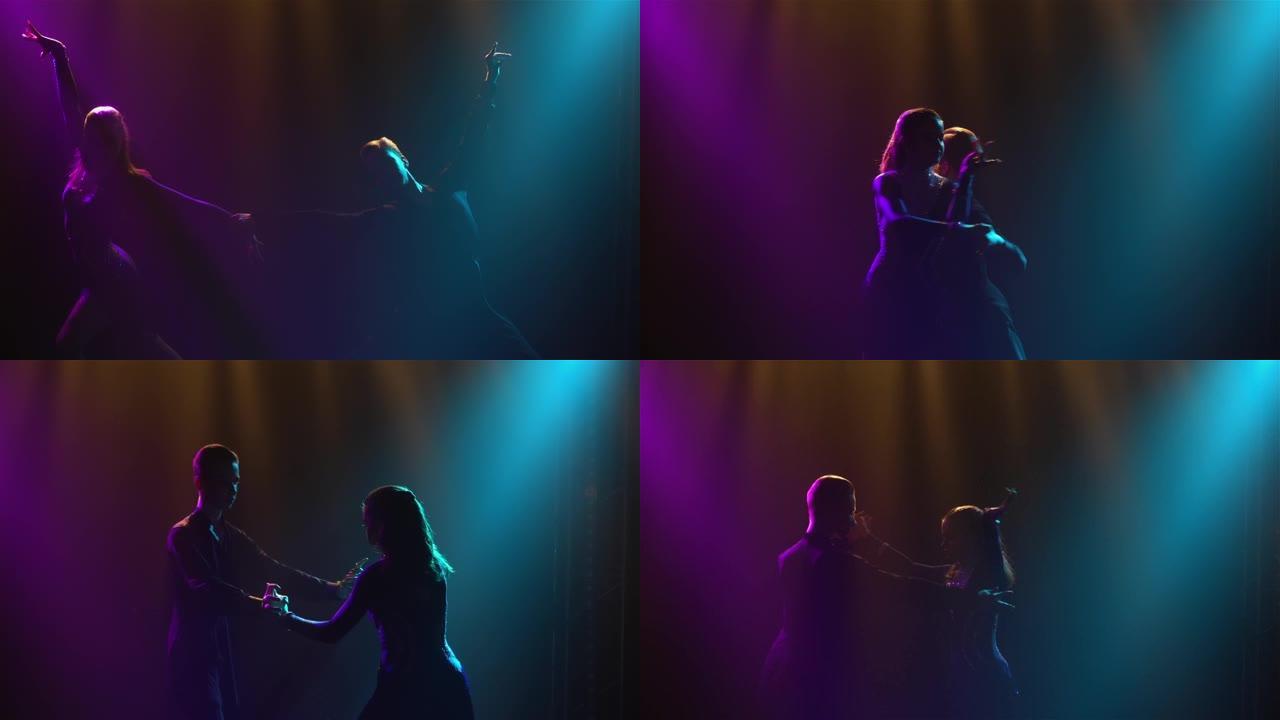 剪影跳舞的夫妇将从黑暗和烟雾中冒出来。男人和女人在工作室光线美丽的蓝紫色光线的背景下热情地跳舞伦巴元