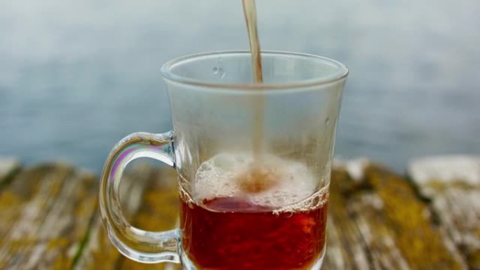旧木皮上的爱尔兰咖啡杯视图。茶被倒入其中。背景下的河流和森林散焦视图。