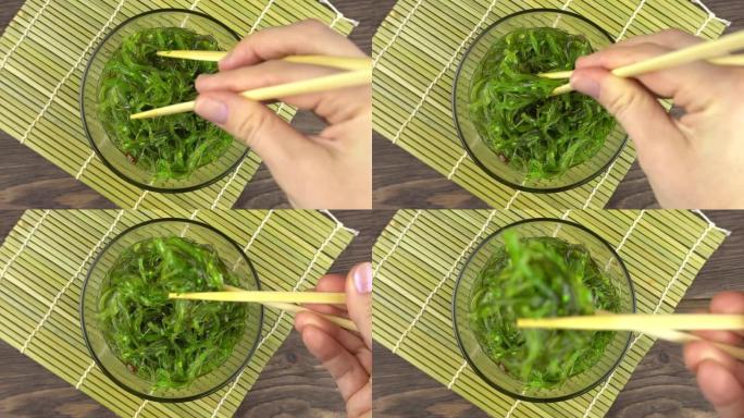Chuka海藻是由女人的手用筷子举起的。玻璃碗中的Chuka海藻站立。
