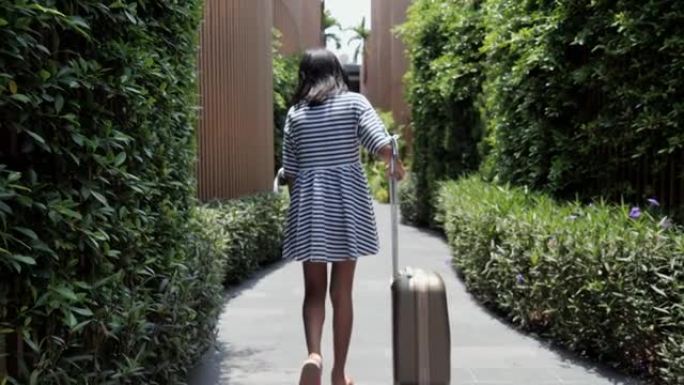 快乐的亚洲女孩和行李在阳光明媚的日子与家人一起度假旅行期间入住/退房后步行到酒店的房间，生活方式理念