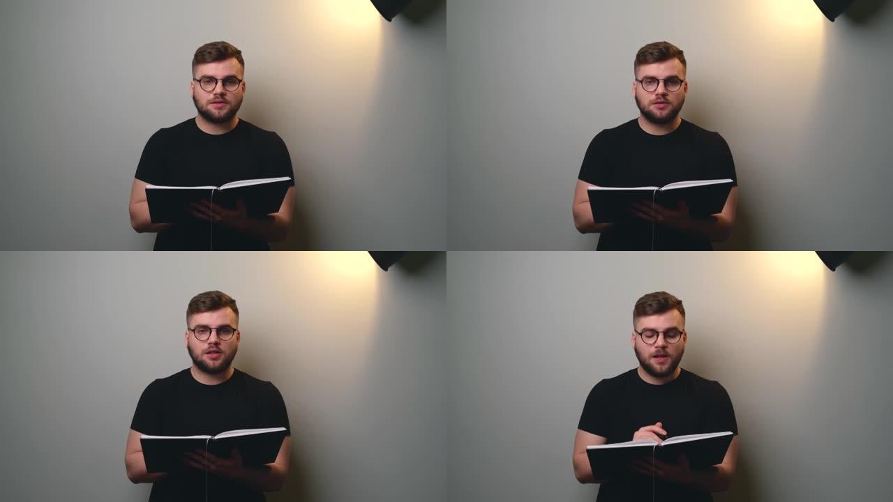 一名白人男子在灰色工作室墙上的镜头前看书的前视视频